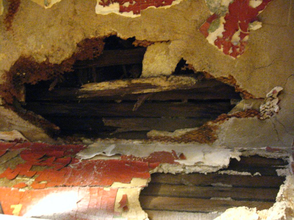 Plaster ceiling with peeling paint and a hole exposing wet wood lath