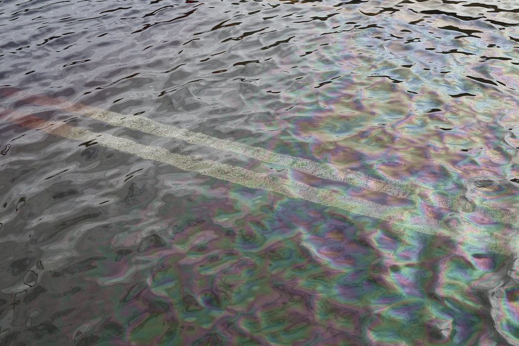 Rainbow petroleum sheen on floodwater covering a roadway