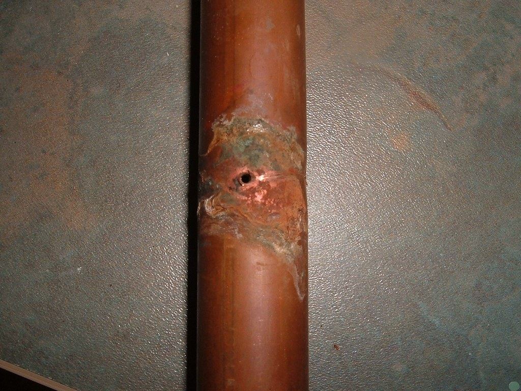 Close-up of a corroded copper water pipe with a small pinhole leak