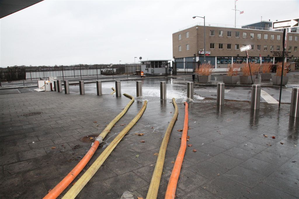 Large pump hoses running across a wet plaza toward a subway station entrance